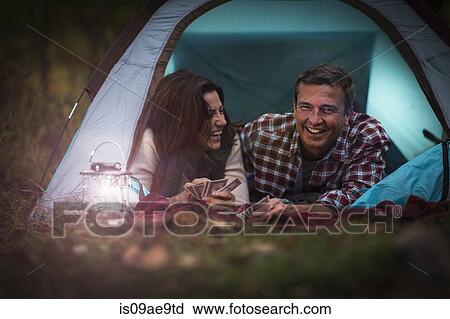 Stock Image - Mature couple lying together in tent, playing card game. Fotosearch