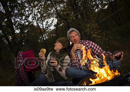 Stock Photo - Mature couple sitting outside tent with barbecue and glass of wine. Fotosearch