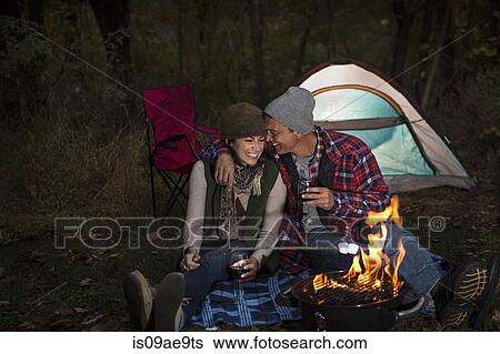 Stock Photograph - Mature couple sitting outside tent with barbecue and glass of wine. Fotosearch