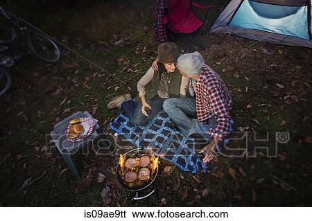 Stock Photograph - Mature couple sitting outside tent with barbecue and glass of wine. Fotosearch