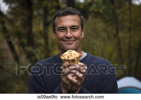 Picture - Mature man in forest holding cupcake. Fotosearch