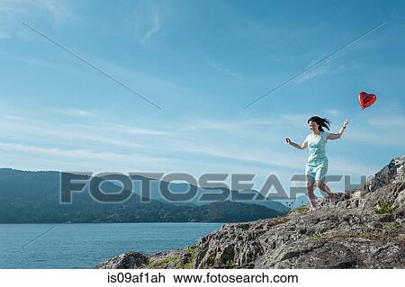 Stock Image - Mature woman pulling heart shaped balloon, Vancouver, Canada. Fotosearch