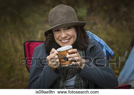 Mature woman sitting on camping chair, drinking hot drink View Large Photo Image Picture - Mature woman sitting on camping chair, drinking hot drink. Fotosearch