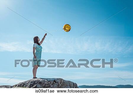 Mature woman standing on rock with golden balloon View Large Photo Image Stock Image - Mature woman standing on rock with golden balloon. Fotosearch