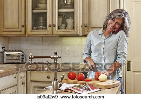 Mature woman using mobile and preparing food in kitchen View Large Photo Image Stock Photo - Mature woman using mobile and preparing food in kitchen. Fotosearch