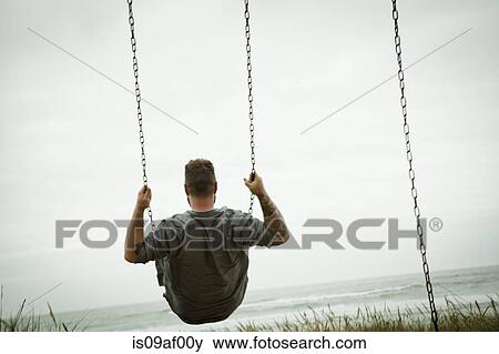 Stock Photo - Mid adult man on beach swing. Fotosearch