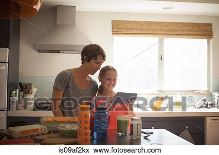 Mother and daughter looking at digital tablet in kitchen View Large Photo Image Stock Photo - Mother and daughter looking at digital tablet in kitchen. Fotosearch