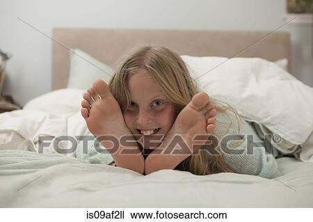 Stock Image - Portrait of girl lying on bed in between feet. Fotosearch