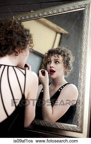 Portrait of young woman applying lipstick in mirror View Large Photo Image Stock Photograph - Portrait of young woman applying lipstick in mirror. Fotosearch