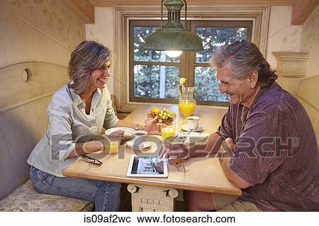 Stock Image - Senior couple enjoying breakfast and using digital tablet. Fotosearch