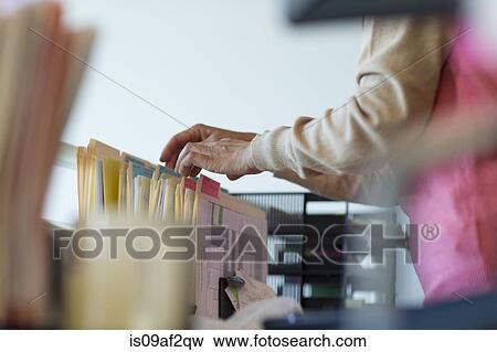 Stock Photo - Senior woman looking through filing cabinet. Fotosearch