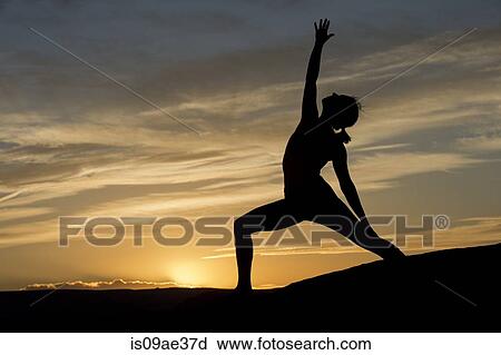 Stock Image - Silhouette of young woman doing yoga, Moab, Utah, USA. Fotosearch