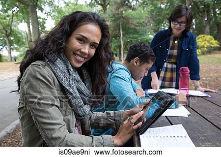 Stock Image - Students sitting at table in park doing homework. Fotosearch