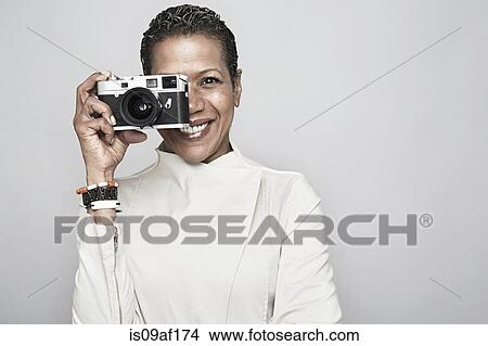 Studio portrait of happy mature woman holding up camera View Large Photo Image Picture - Studio portrait of happy mature woman holding up camera. Fotosearch