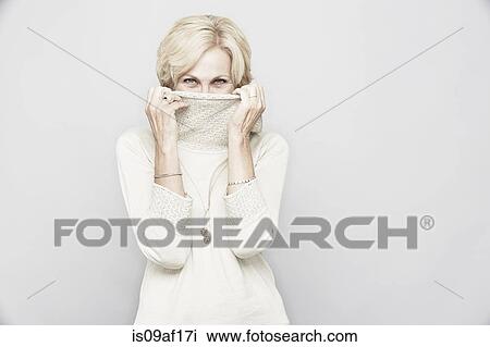 Stock Image - Studio portrait of senior woman hiding behind roll neck. Fotosearch