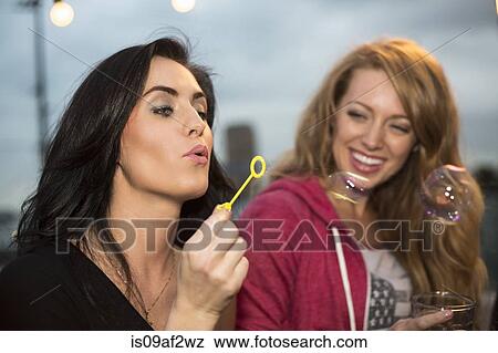 Two female friends blowing bubbles at rooftop party View Large Photo Image Stock Photo - Two female friends blowing bubbles at rooftop party. Fotosearch