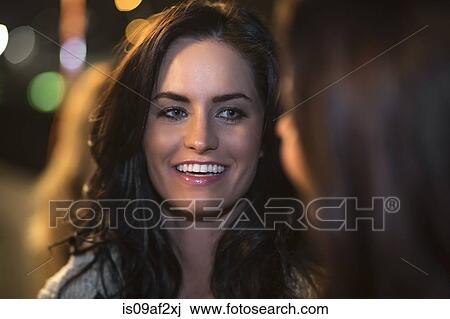 Stock Image - Two female friends chatting at rooftop party. Fotosearch