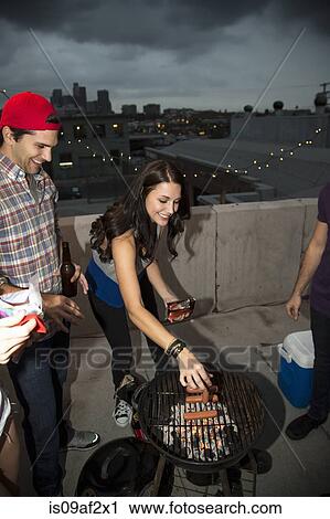 Stock Image - Young adult friends barbecuing at rooftop party. Fotosearch