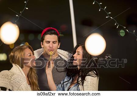 Stock Photography - Young adult friends blowing bubbles at rooftop party. Fotosearch