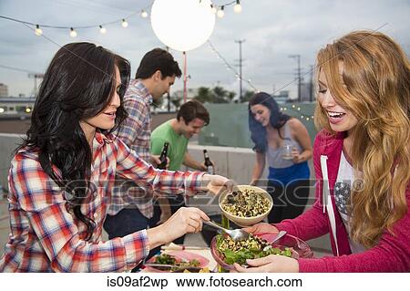 Stock Photography - Young adult friends enjoying food at barbeque. Fotosearch