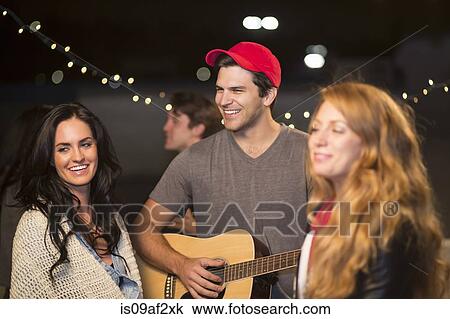 Young adult friends enjoying guitar music at rooftop party View Large Photo Image Stock Image - Young adult friends enjoying guitar music at rooftop party. Fotosearch