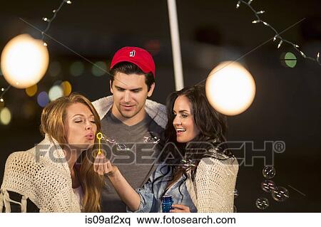 Young adult friends fooling around blowing bubbles at rooftop party View Large Photo Image Stock Photography - Young adult friends fooling around blowing bubbles at rooftop party. Fotosearch