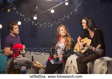 Young adult friends listening to guitar at party View Large Photo Image Stock Image - Young adult friends listening to guitar at party. Fotosearch