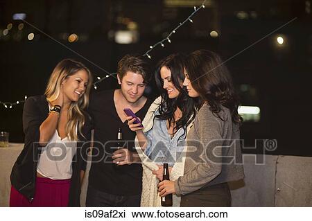 Young adult friends looking at mobile phone at rooftop party View Large Photo Image Stock Image - Young adult friends looking at mobile phone at rooftop party. Fotosearch