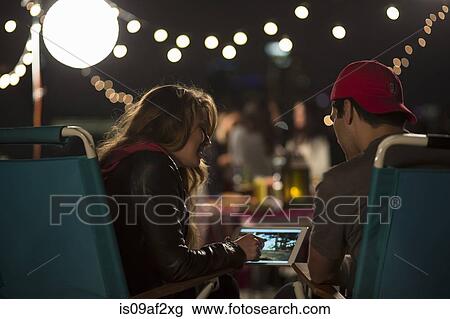 Stock Image - Young couple looking at digital tablet at rooftop barbecue. Fotosearch