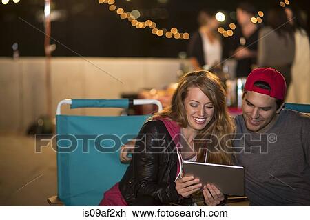 Stock Image - Young couple using digital tablet at rooftop barbecue. Fotosearch