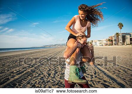 Stock Photo - Young man carrying girlfriend on shoulders on San Diego beach. Fotosearch