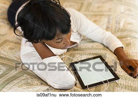 Young woman lying on bed using digital tablet View Large Photo Image Stock Photograph - Young woman lying on bed using digital tablet. Fotosearch