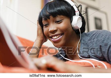 Stock Photograph - Young woman lying on sofa using digital tablet. Fotosearch