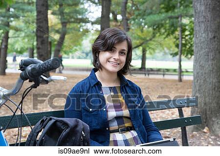 Stock Image - Young woman sitting in park using digital tablet. Fotosearch