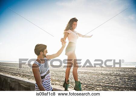 Stock Photo - Young woman walking along wall holding boyfriend's hand for balance. Fotosearch