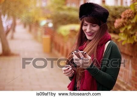 Young woman wearing winter clothing, holding smartphone View Large Photo Image Stock Photo - Young woman wearing winter clothing, holding smartphone. Fotosearch