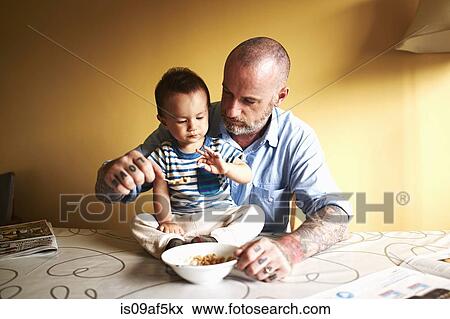 Baby boy sitting on table having cereal with father View Large Photo Image Stock Photo - Baby boy sitting on table having cereal with father. Fotosearch