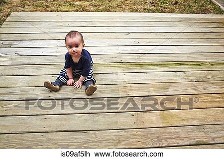 Stock Image - Baby boy sitting on wooden decking in garden. Fotosearch