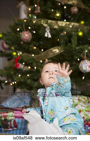 Stock Photo - Baby girl reaching up, christmas tree in background. Fotosearch