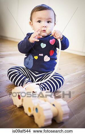 Picture - Baby girl sitting on floor with toy. Fotosearch