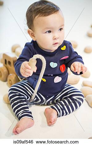 Baby girl sitting on floor with toy View Large Photo Image Stock Photograph - Baby girl sitting on floor with toy. Fotosearch