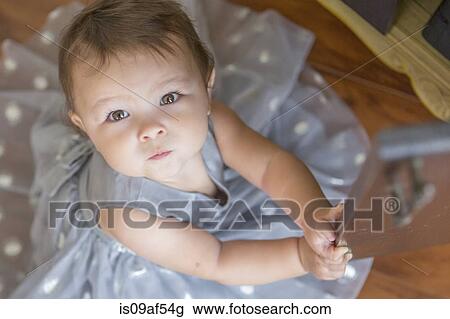 Stock Image - Baby girl wearing party dress, looking up. Fotosearch
