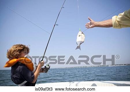 Stock Image - Boy reeling in fish on boat, Falmouth, Massachusetts, USA. Fotosearch