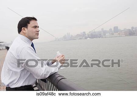Businessman leaning on rail holding bottle of water View Large Photo Image Stock Image - Businessman leaning on rail holding bottle of water. Fotosearch