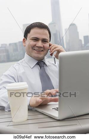 Stock Image - Businessman using laptop outdoors, Jersey City, New Jersey, USA. Fotosearch