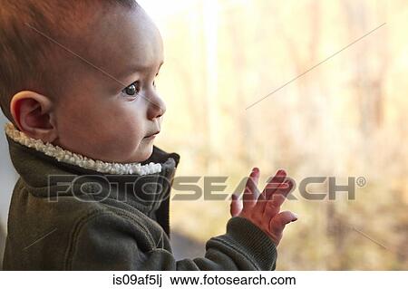 Stock Image - Close up of baby boy looking out of window. Fotosearch