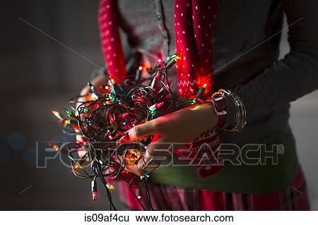 Stock Photograph - Close up of young woman holding tangle of christmas lights. Fotosearch