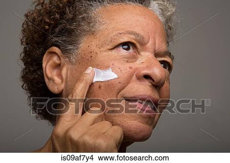 Picture - Close up studio portrait of senior woman applying face cream. Fotosearch