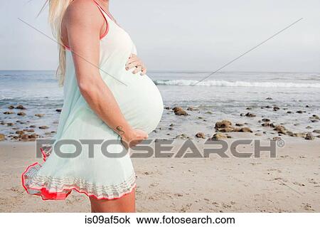Stock Image - Cropped image of pregnant young woman on beach. Fotosearch