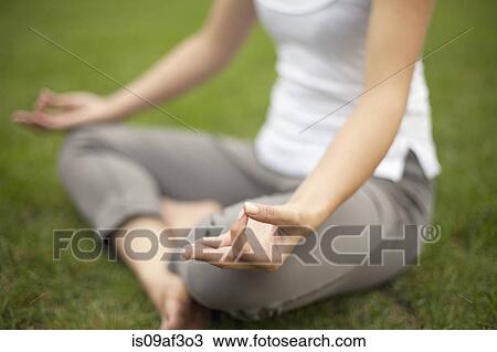 Stock Image - Cropped image of young woman in park practicing lotus position. Fotosearch